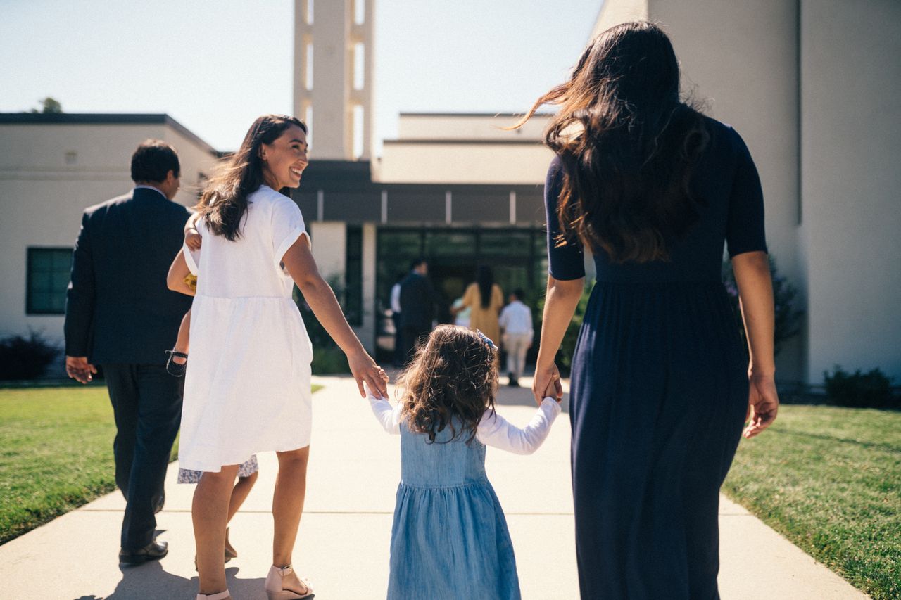 A small girl reaches for a woman’s hand as they enter a church meetinghouse